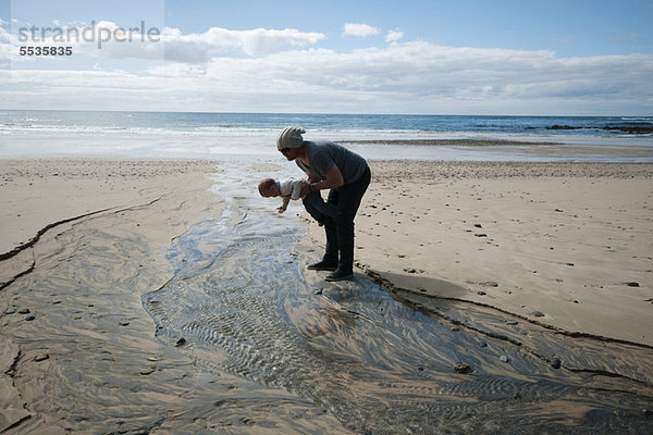 Vater und Kleinkind beim Blick auf den geriffelten Sand am Strand