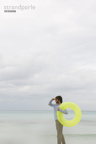 Junger Mann mit aufblasbarem Schwimmring  Blick in die Ferne