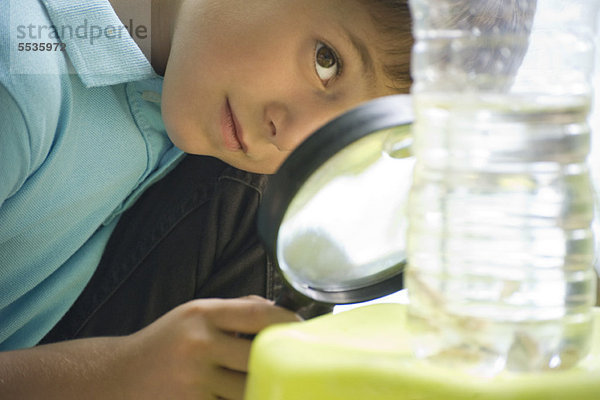 Junge studiert Wasserflasche mit Lupe