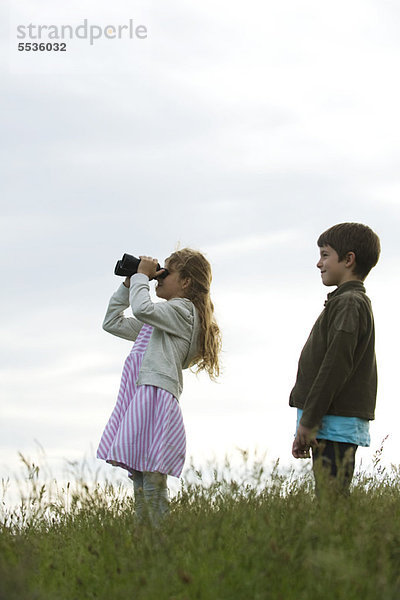 Mädchen im Feld stehend mit Junge  durchs Fernglas schauend