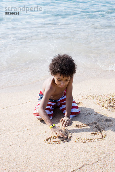 Junge schreibt im Sand am Strand