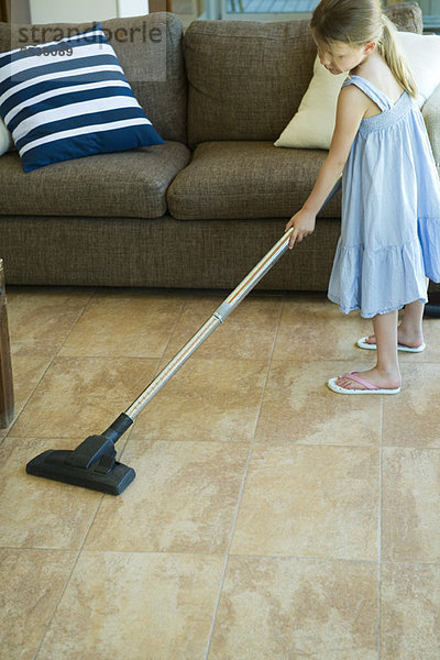 Kleines Mädchen reinigt Wohnzimmerboden mit Staubsauger