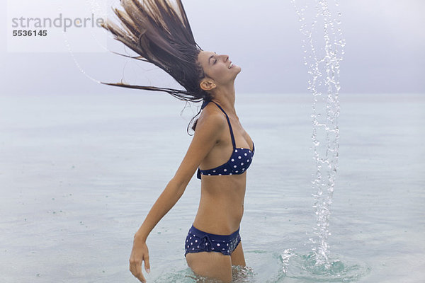 Frau wirft nasse Haare ins Wasser