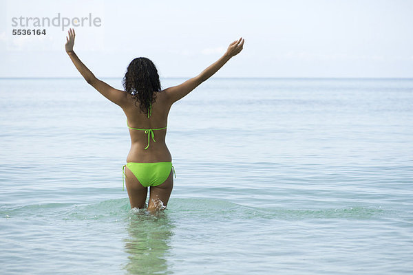 Frau im Bikini stehend im Meer mit ausgestreckten Armen  Rückansicht