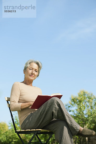 Seniorin im Freien sitzend mit Buch  Portrait