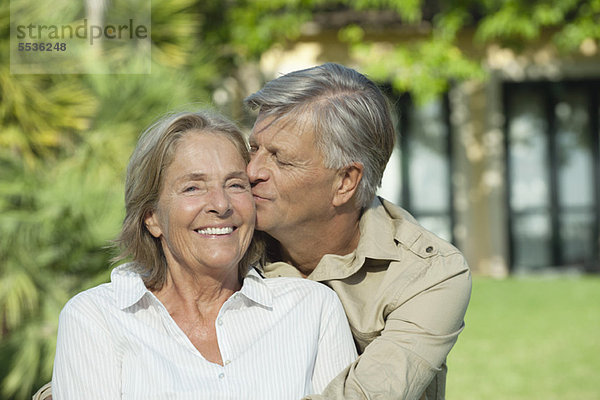 Senior Mann  der seine Frau auf die Wange küsst.
