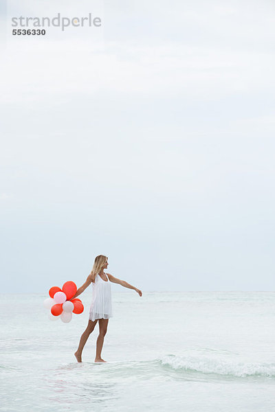 Eine Frau  die auf dem Wasser geht und einen Haufen Luftballons trägt.