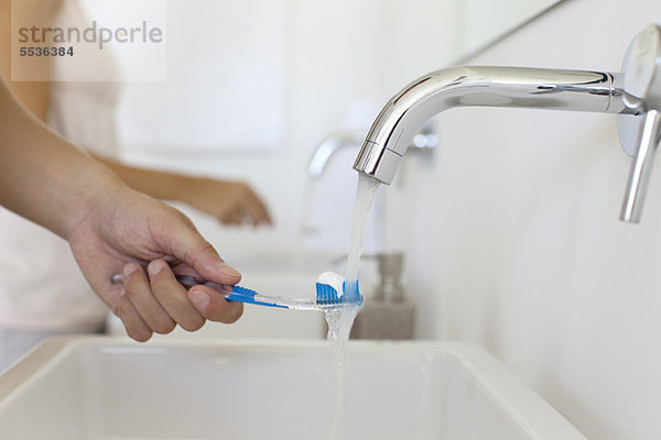 Mann hält Zahnbürste unter Wasserhahn  abgeschnitten