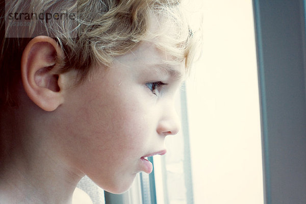 Kleiner Junge  der aus dem Fenster schaut.