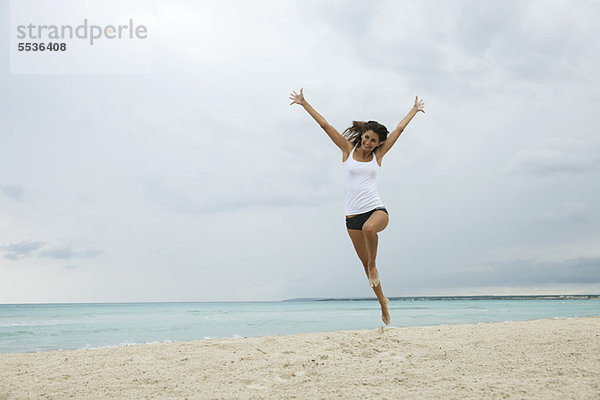 Junge Frau beim Luftspringen am Strand