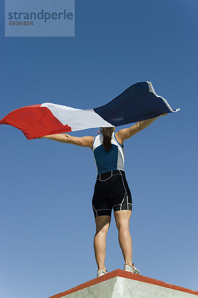 Eine Athletin auf dem Siegerpodest  die die französische Flagge hochhält.