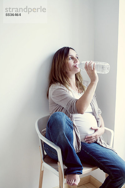 Schwangere Frau trinkt Wasser aus der Flasche