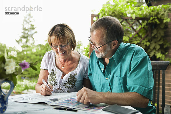 Glückliches Seniorenpaar löst gemeinsam Kreuzworträtsel in der Zeitung