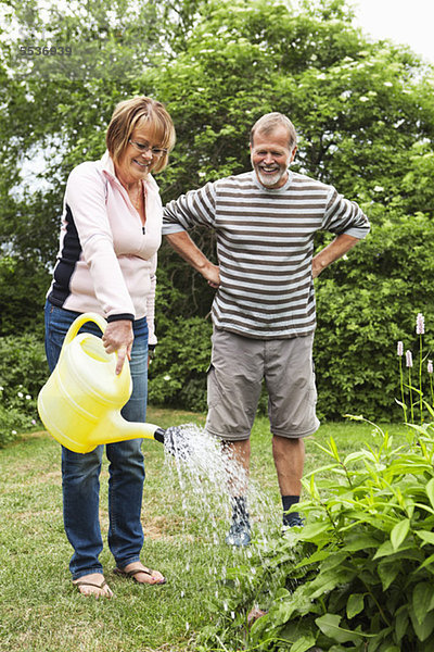 Ältere Frau  die Pflanzen gießt  während der Mann mit den Händen an der Hüfte zuschaut.