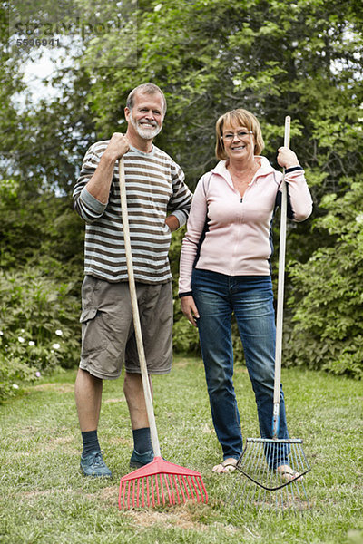 Aktives Seniorenpaar mit Rechen im Rasen stehend