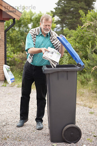 Älterer Mann wirft Zeitung in die Mülltonne