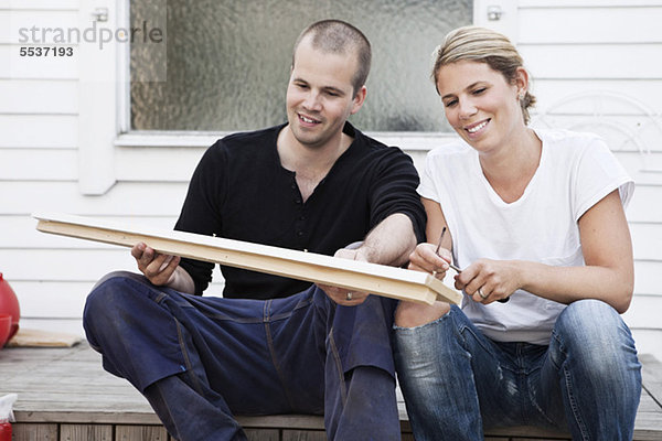 Glückliches Paar sitzt vor dem Haus und hält die Planke.