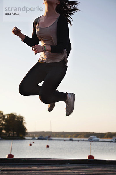 Teenagermädchen genießt Freiheit beim Springen am Pier
