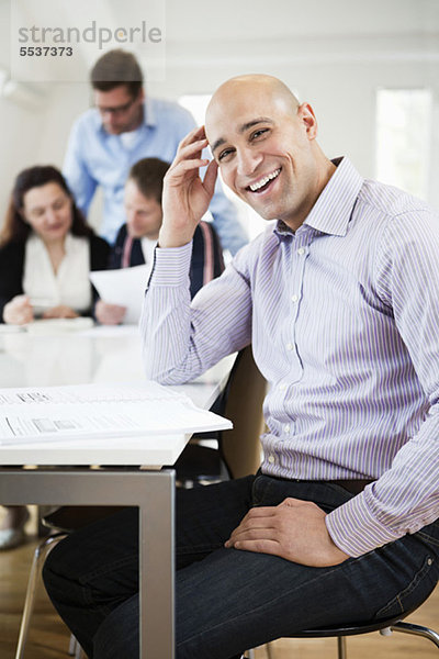 Porträt eines mittelgroßen Mannes  der lächelt  mit einem Geschäftstreffen im Hintergrund