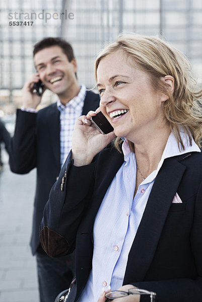 Glückliche Frau am Telefon mit Geschäftsmann im Hintergrund