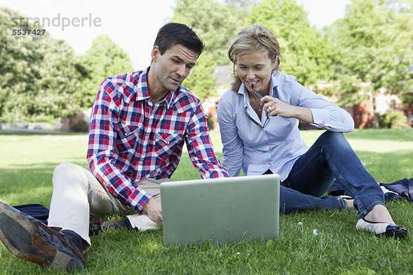 Geschäftsleute sitzen auf Rasen mit Laptop im Park