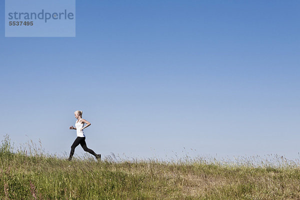 Volle Länge der jungen Frau beim Joggen gegen den blauen Himmel