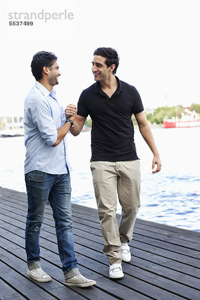 Zwei männliche Freunde halten sich an den Händen  während sie zusammen auf dem Pier gehen.