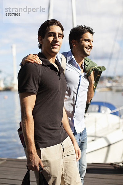 Junge männliche Freunde  die auf dem Pier mit dem Arm herumlaufen.