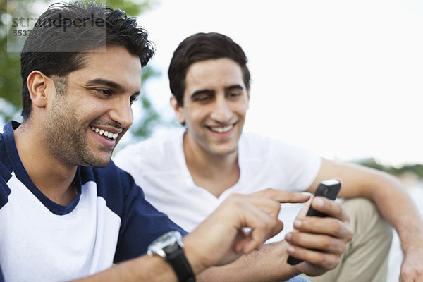 Nahaufnahme eines jungen Mannes  der sein Handy benutzt  während ein Freund auf der Suche ist.