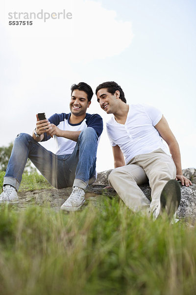 Junge männliche Freunde  die sich ein Handy im Freien teilen