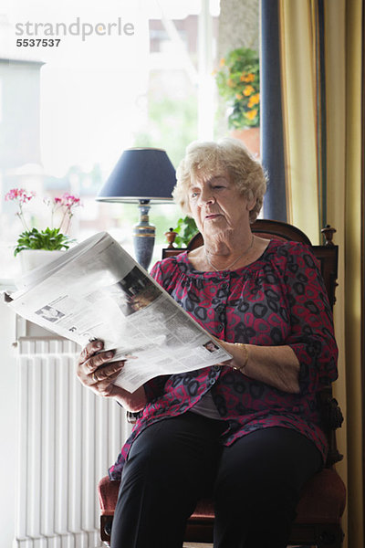 Entspannte Seniorin beim Zeitungslesen zu Hause