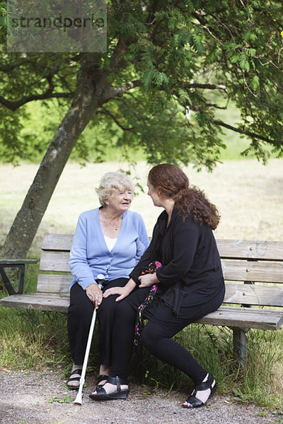 Großmutter und Enkelin sitzen zusammen auf der Parkbank.