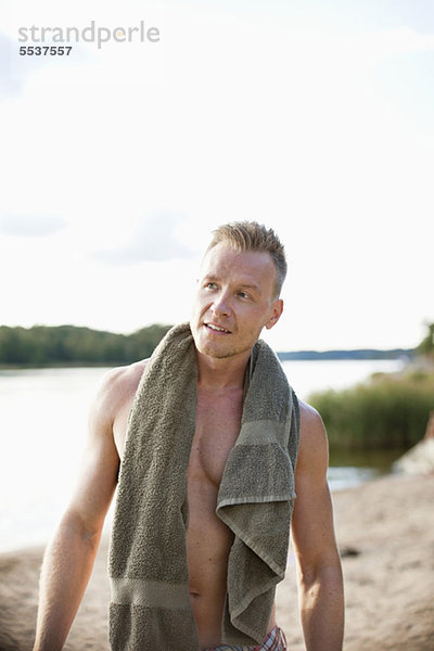 Vorderansicht eines erwachsenen Mannes mit Handtuch am Strand