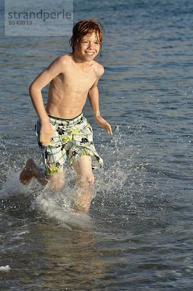 Junge läuft im Wasser am Strand am Meer