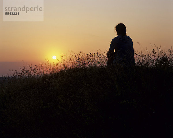 Silhouette einer jungen Frau die sitzend in den Sonnenuntergang schaut  Thüringen  Deutschland  Europa