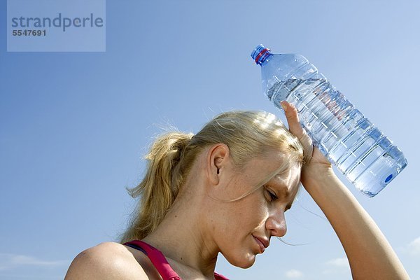 Junge Frau hält eine Flasche Wasser unter blauem Himmel