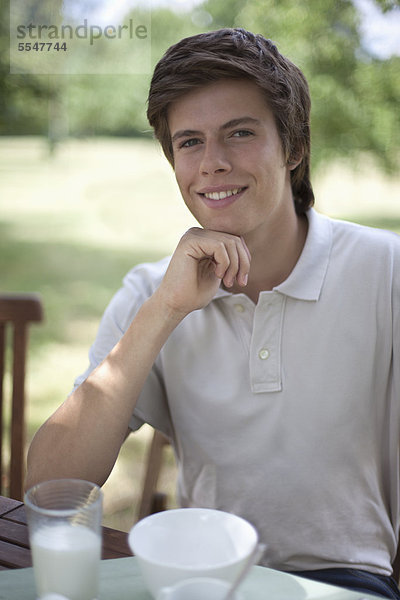 Lächelnder junger Mann sitzt am Gartentisch