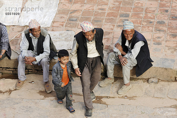 Männer mit traditioneller Kopfbedeckung und Junge auf dem Taumadhi-Platz  Bhaktapur  Kathmandu-Tal  Nepal  Asien