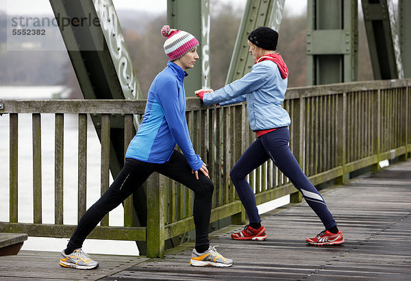 Zwei junge Frauen bei Dehnungsübungen nach dem Laufen im Winter  mit wind- und wasserdichter Funktionsbekleidung