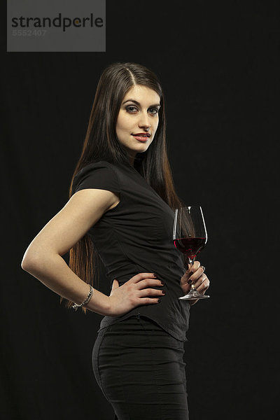 Junge Frau in Abendkleid hält ein Glas Rotwein