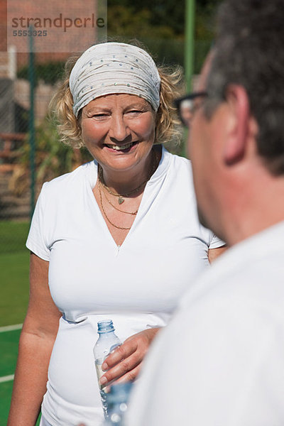 Leitende und ältere Erwachsene genießen Getränk am Tennisplatz