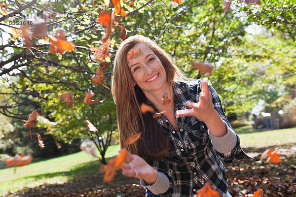 Frau wirft Herbstlaub in die Luft