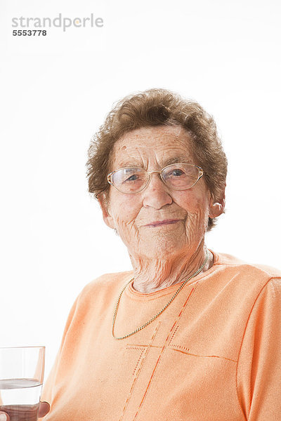 Lächelnde alte Frau mit Brille hält ein Glas Wasser  Portrait