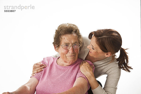 Lächelnde reife Frau umarmt sitzende alte Frau