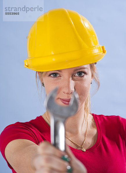 Junge Frau mit Bauhelm hält einen Schraubenschlüssel