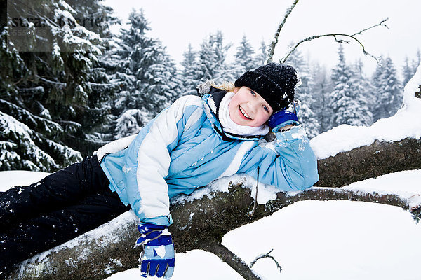 Mädchen auf einem umgefallenen Baumstamm im Schnee