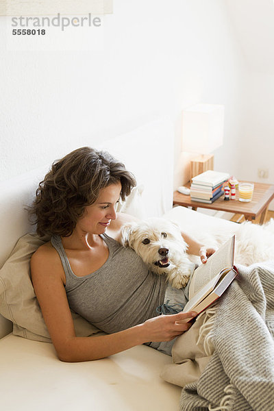 Frau liest mit Hund im Bett