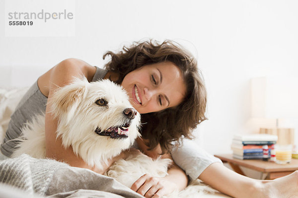 Lächelnde Frau streichelt Hund im Bett