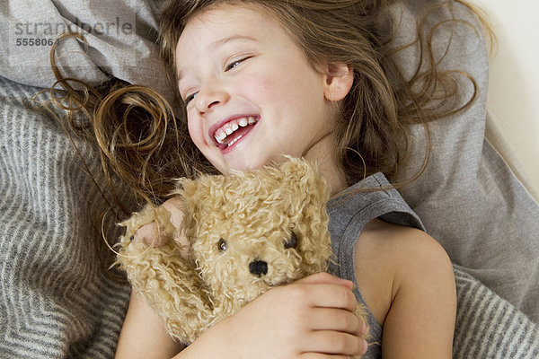 Lächelndes Mädchen mit Teddybär im Bett