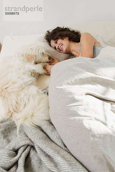 Frau entspannt im Bett mit Hund